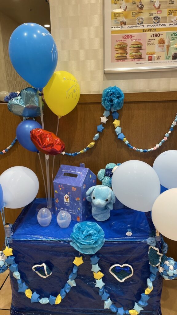 スタッフの方々による手作りの青いマックの日の装飾と募金箱