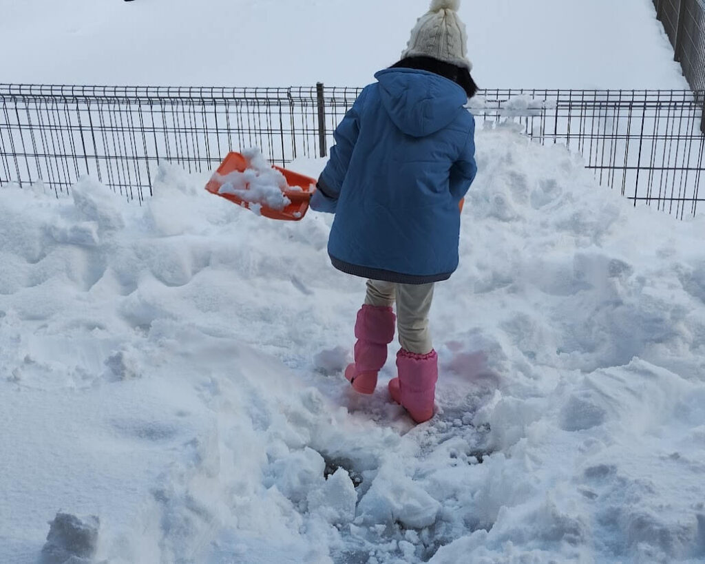 冬の感覚統合遊び。降り積もった雪をスコップを握って押し引きしている様子。この動作で、身体の位置や動きの認識を向上させる