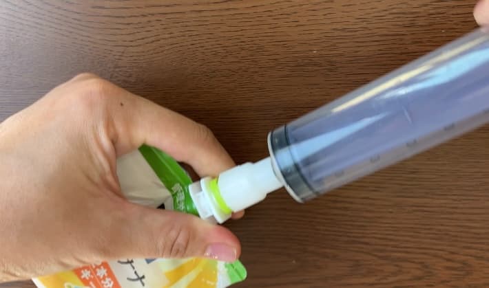 市販のパウチ型飲料と、注入用シリンジを接続するコネクタをパウチ内の空気を抜いて接続している様子