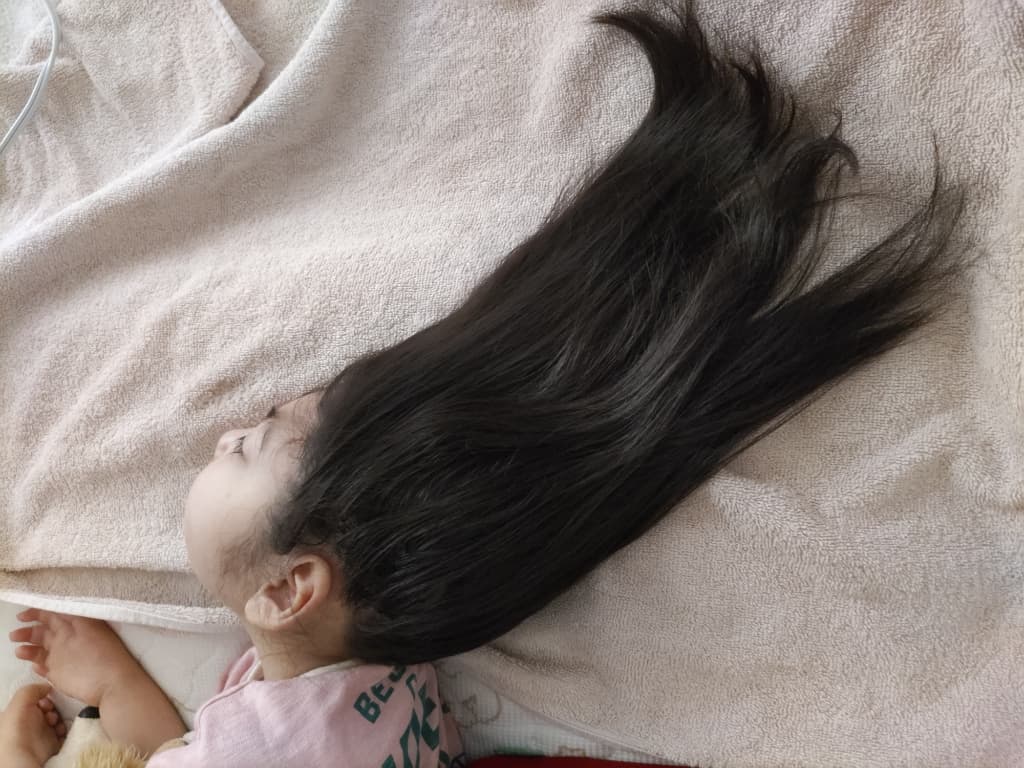 髪の毛の長い女の子がタオルの上に頭を置いて横になっている