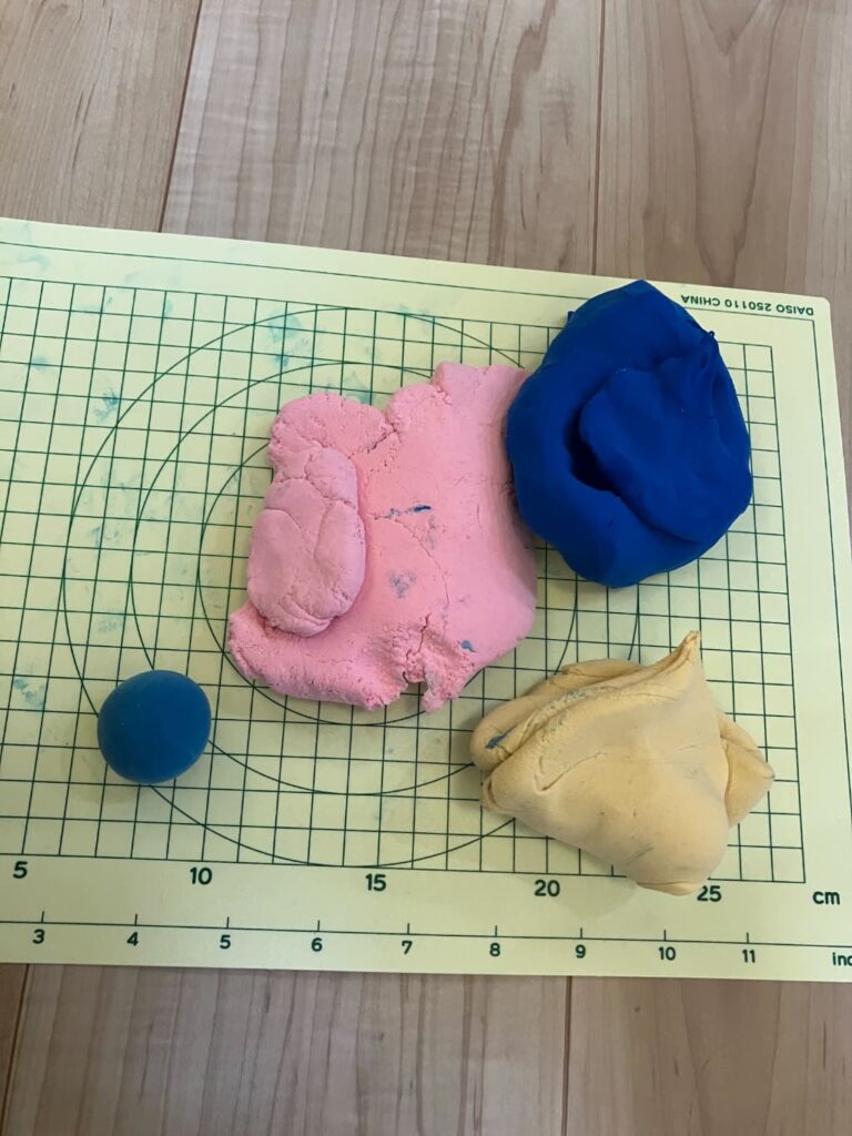 粘土用のマットの上に、青・黄色・ピンクの粘度が置いてあるところ