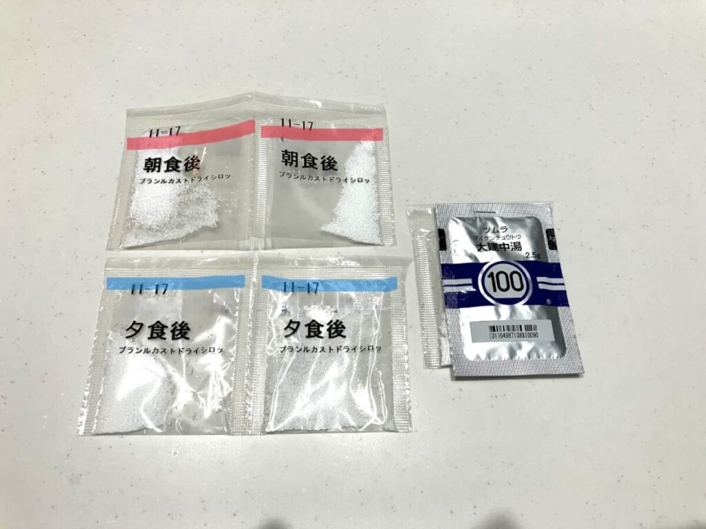 朝食後・夕食後に服用する粉薬を小分けにした袋に内服時間ごとに赤・青で色分けしたマーカーが引いてある。漢方と内服薬の小袋が一緒にホッチキス止めされている。の個包装を並べた写真