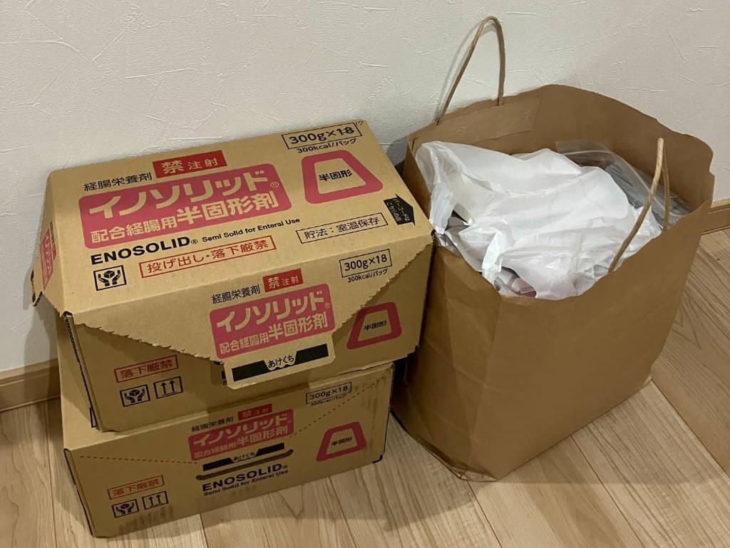 経腸栄養剤イノソリッドの段ボール箱と、たくさんの内服薬が入った紙袋が床に置いてある