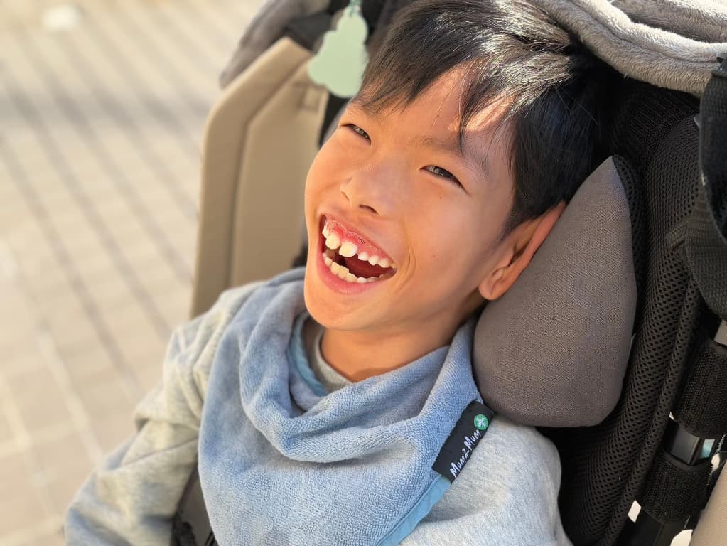 黒い車椅子に乗った小学校低学年の男の子が口を開けた笑顔でこちらを見ているところ