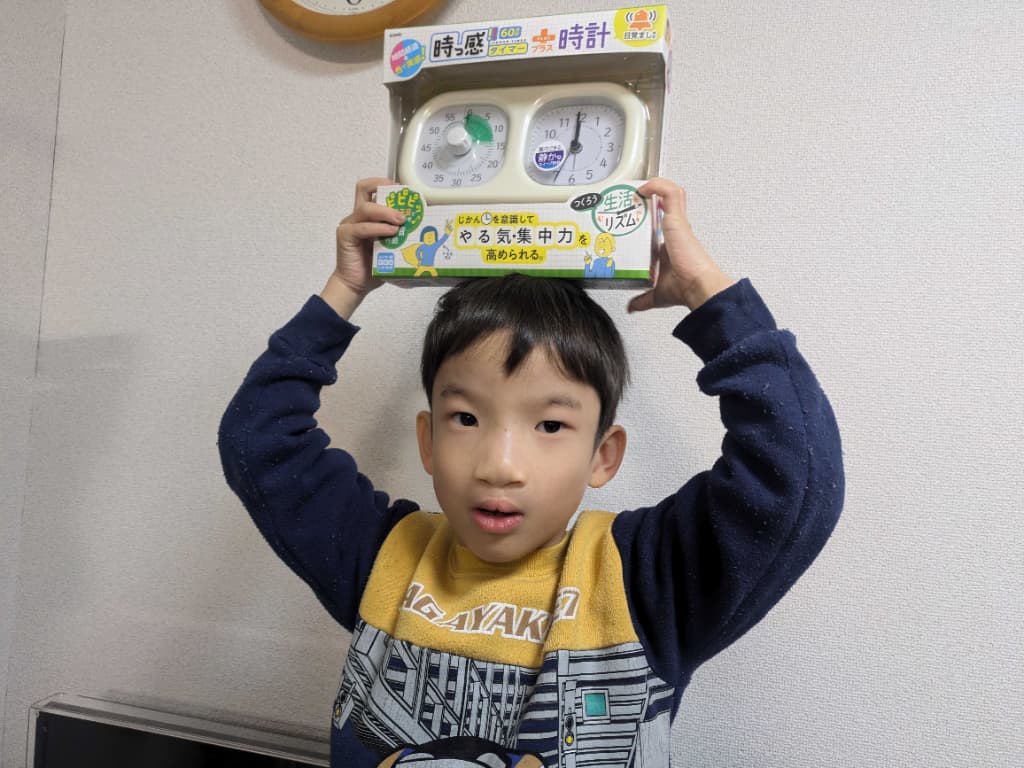 白色の時計を頭の上に掲げている男の子