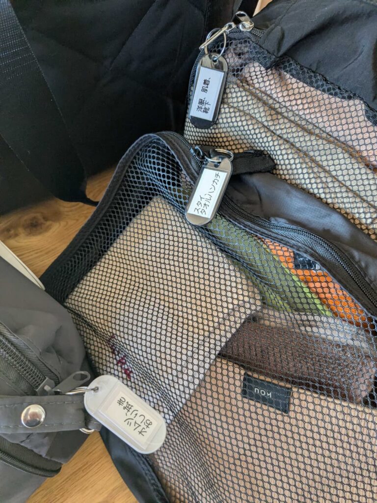メッシュ素材のポケットが付いたバッグの中に複数の袋が入っており、それぞれに文字入りの名札が付いている