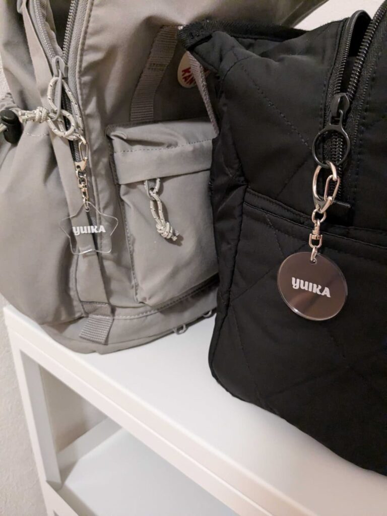 グレーのリュックと黒いバッグが並んで置かれ、それぞれに丸い名前入りのタグが付いている