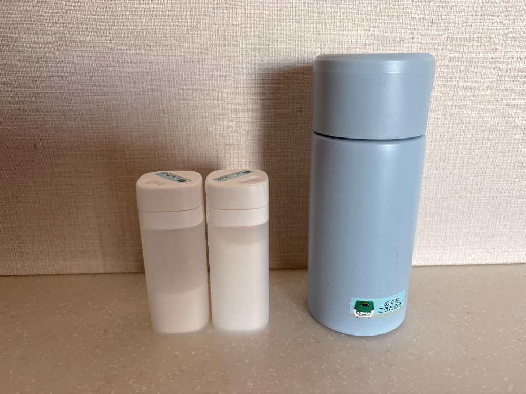 白い小型ボトル2本と、水色の水筒が横に並んで置かれている