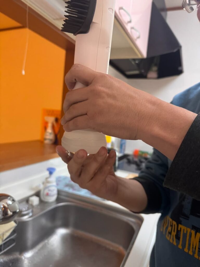 キッチンのシンク前で手に持ったSUSUGUのヘッド部分を操作している様子。ブラシ付きの本体を組み立てている手元が写っている