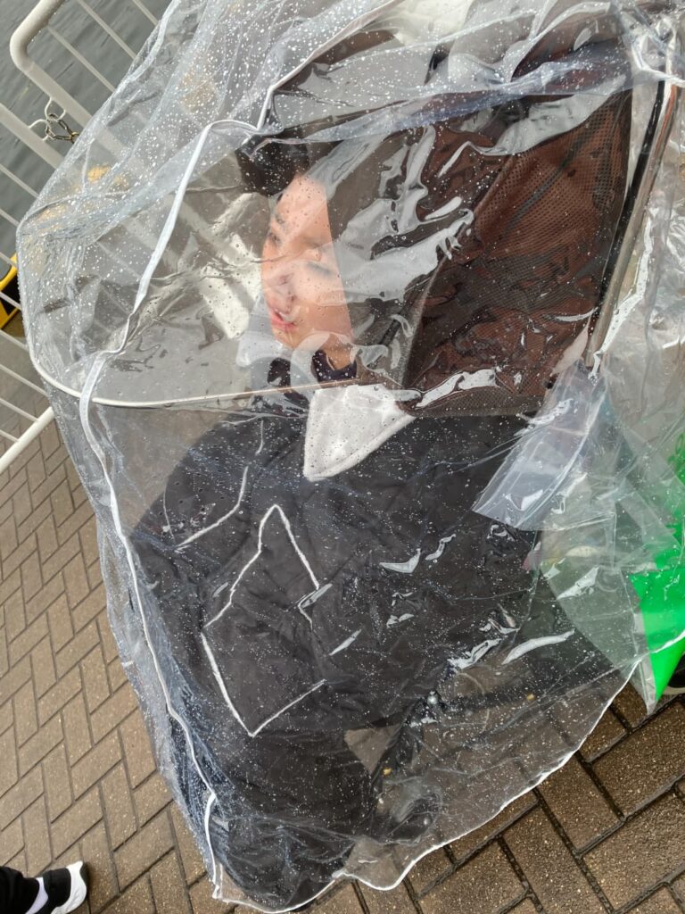 透明なレインカバーを装着したバギーに座る男の子。雨や風を防ぐため、バギー全体が透明カバーで覆われている