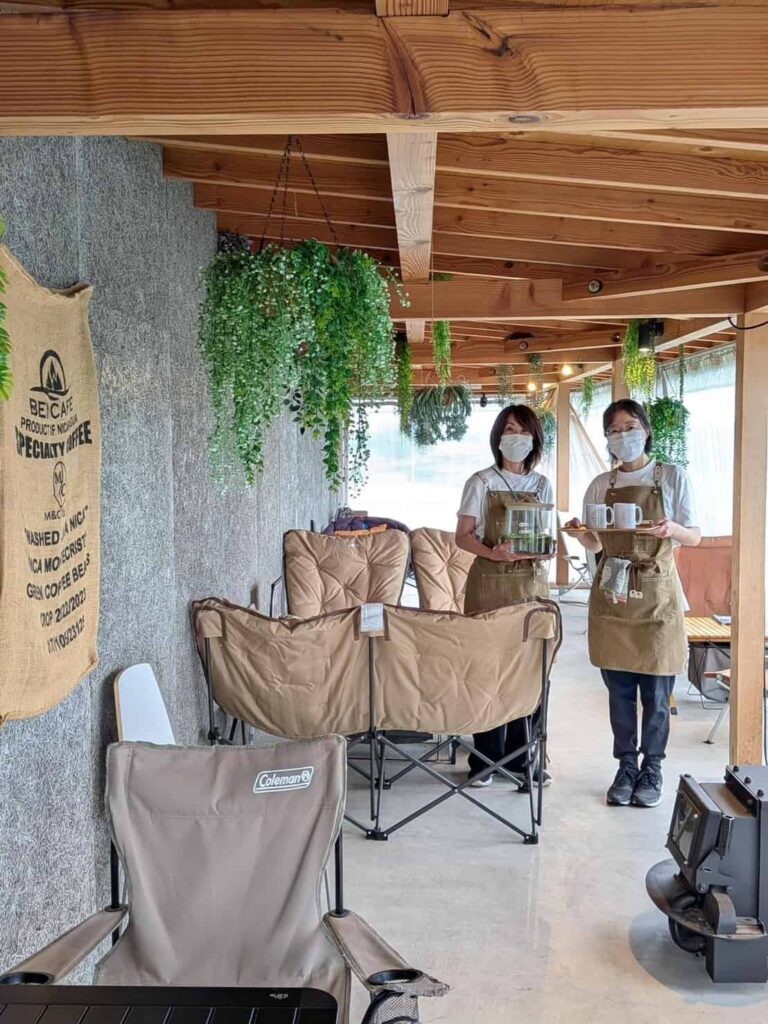 カフェの店内で、ベージュのエプロンを付けた店員の女性二人が並んで立っている様子
