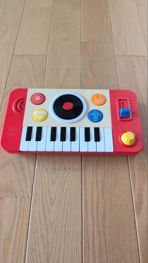 黒白の鍵盤、中央の黒いレコード型ボタン、青いスライダー、黄色い音量ダイヤルが付いた赤い子ども用キーボード