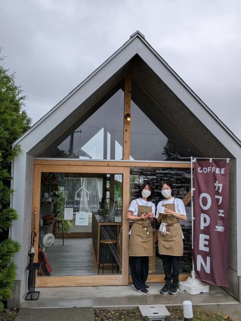 カフェの店の前でベージュのエプロンを付けた女性の店員が2人並んでいる様子