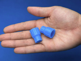 手のひらの上に載せた、青いパウチ専用コネクタ「つなぐっど」2個。両端の接続部分の形状と、手のひらに収まるサイズ感がわかる。